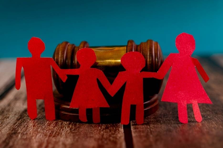 Family law and legal protections are represented in this image. Cutout red paper figures of a family stand in front of a wooden judge's gavel.